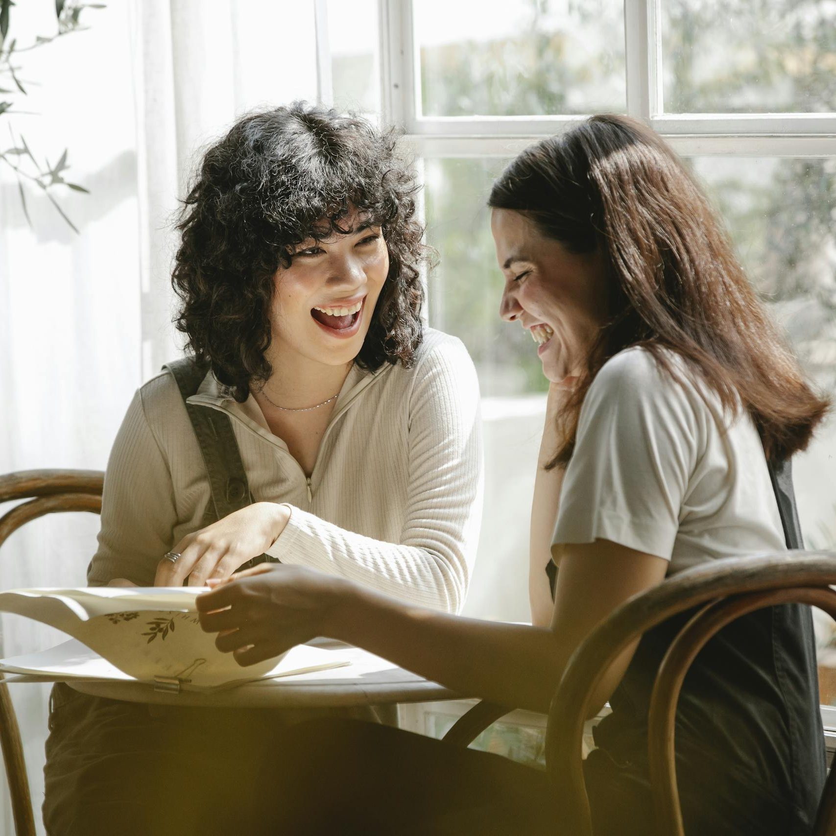 Laughing multiracial female colleagues wearing uniform flipping pages of papers while discussing work together